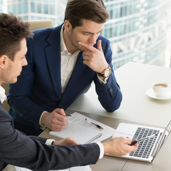 Business partners using laptop while working together on important corporate project in office. Businessman attentively listening to adviser Investment specialist making presentation of promising deal